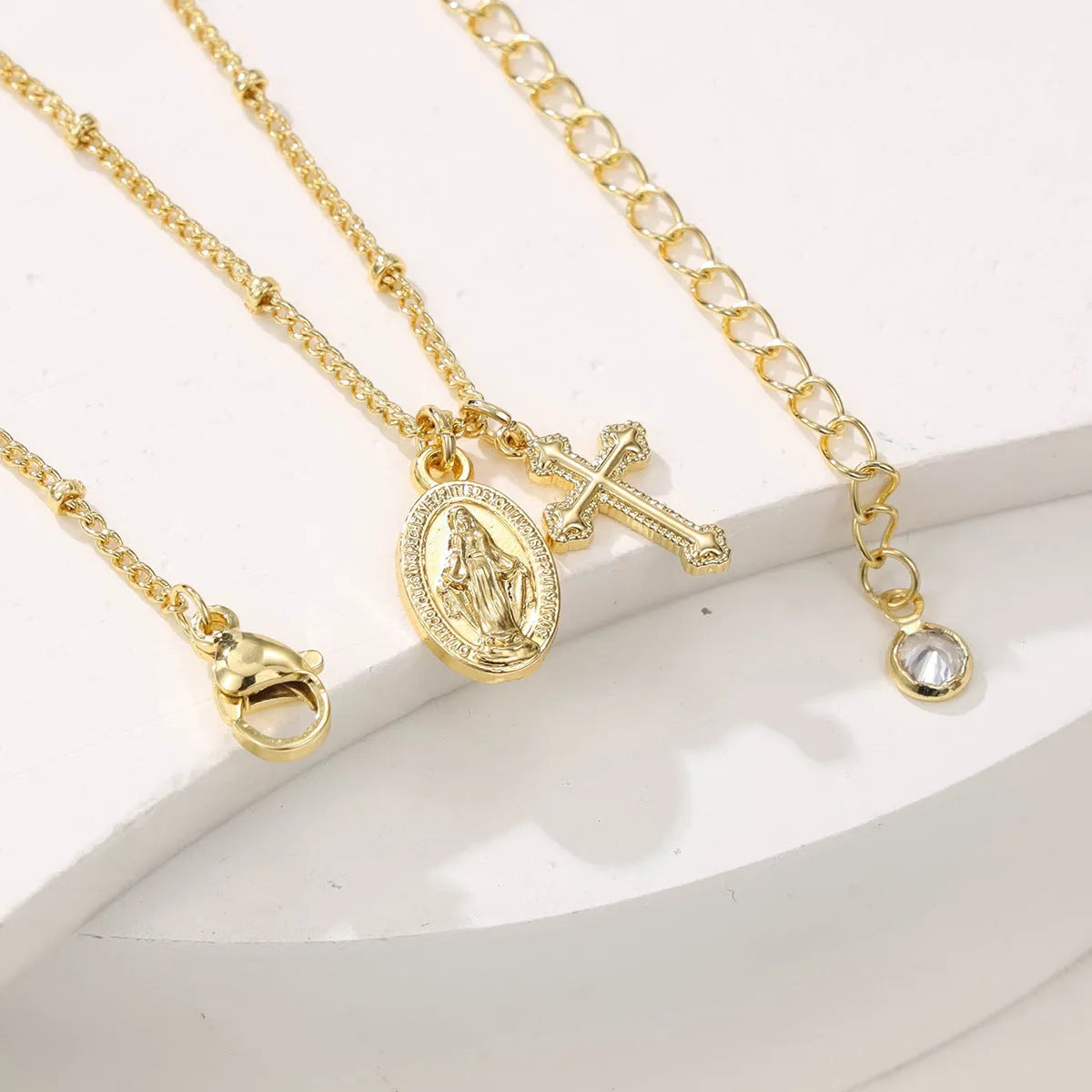 Gold geometric cross pendant necklace with Virgin Mary design on a chain.