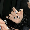 Hand-painted black false nails with pink peach hearts, XINGX text, bows, and a cat's eye shimmer effect.