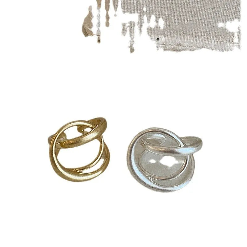 Geometric open ring for women with three-dimensional interlaced design in matte gold or silver metal.