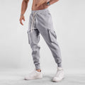 Men's loose light grey cotton sports trousers with ankle ties and multiple pockets laid flat.