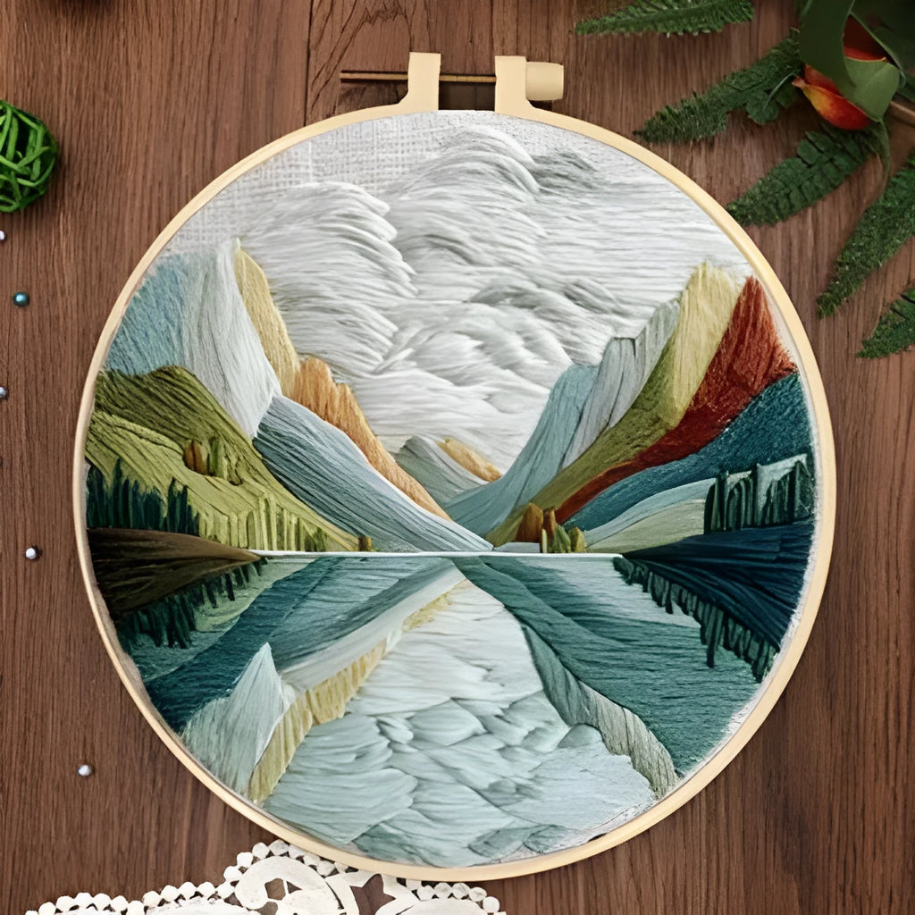 Landscape embroidery DIY kit with cotton fabric, printed pattern, embroidery frame, needles, and thread on wooden surface