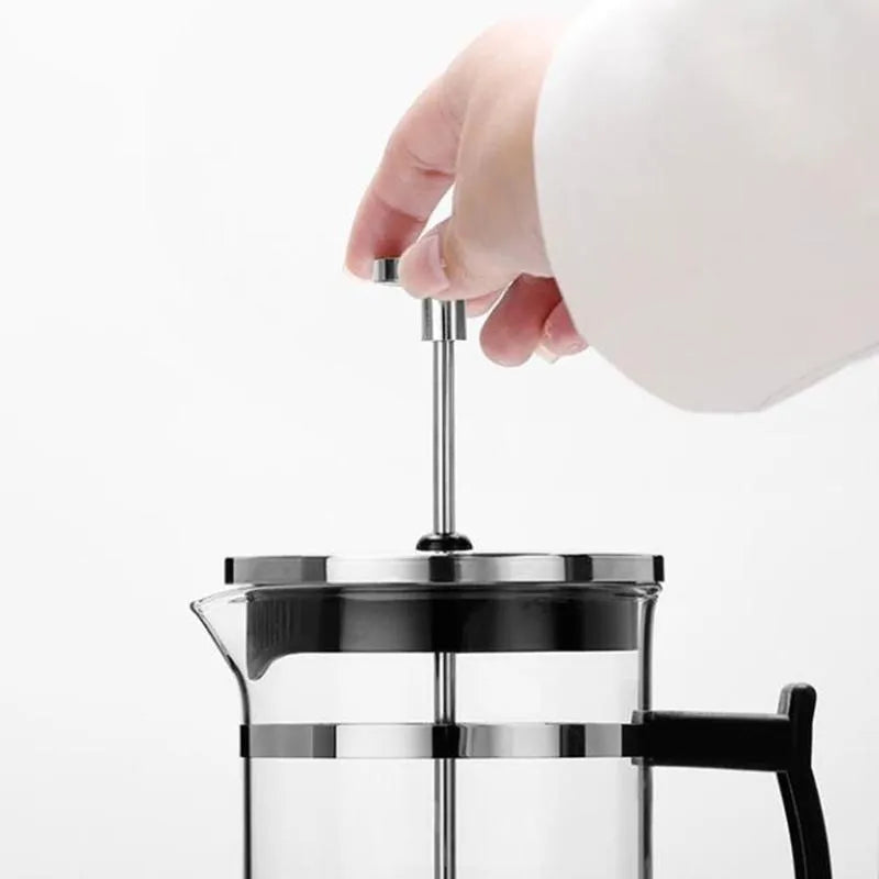 Compact stovetop moka pot coffee maker with glass top and stainless steel base.