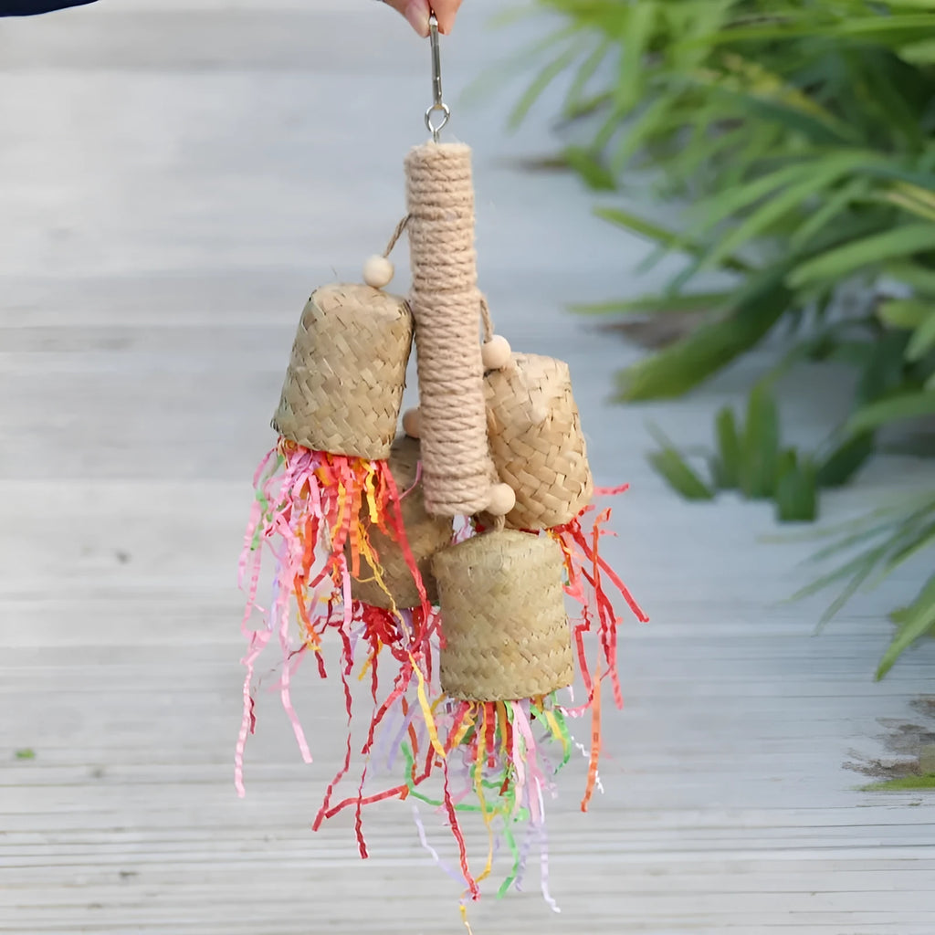 Wood and sisal rope parrot toy with colourful shredded paper hanging inside a bird cage.