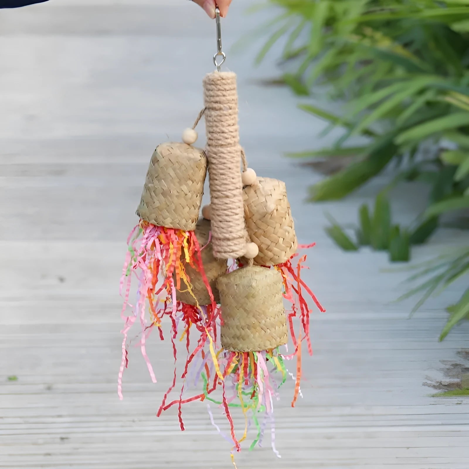 Wood and sisal rope parrot toy with colourful shredded paper hanging inside a bird cage.