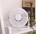 Compact black USB desk fan with adjustable tilt angle on a wooden desk next to a laptop