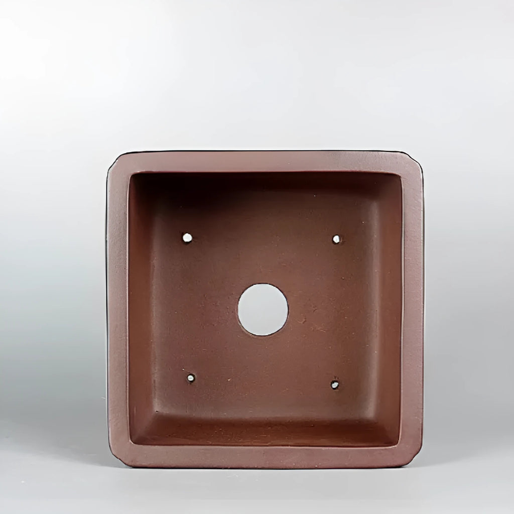 Handmade brown antique flower pot made from purple clay on a wooden surface.