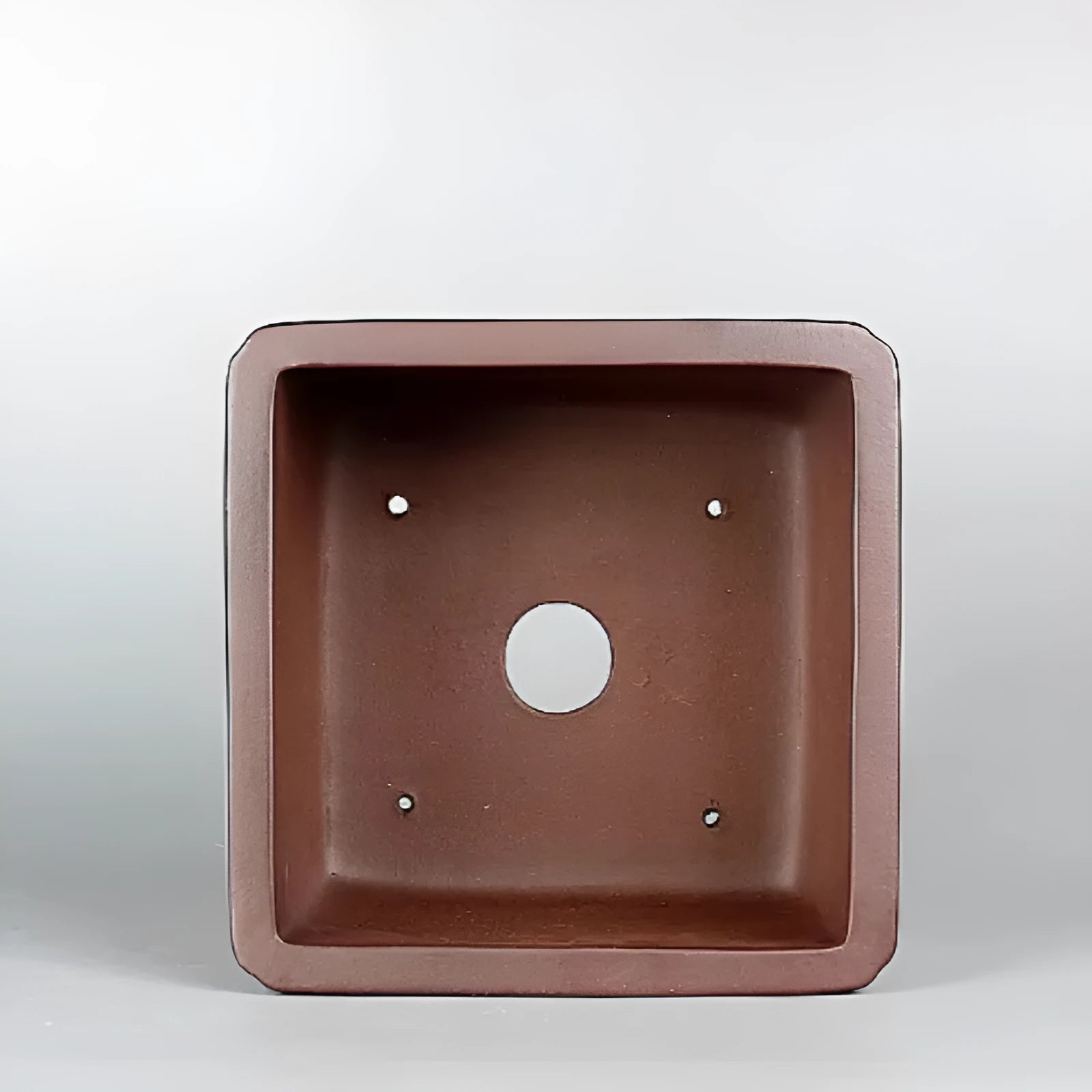 Handmade brown antique flower pot made from purple clay on a wooden surface.