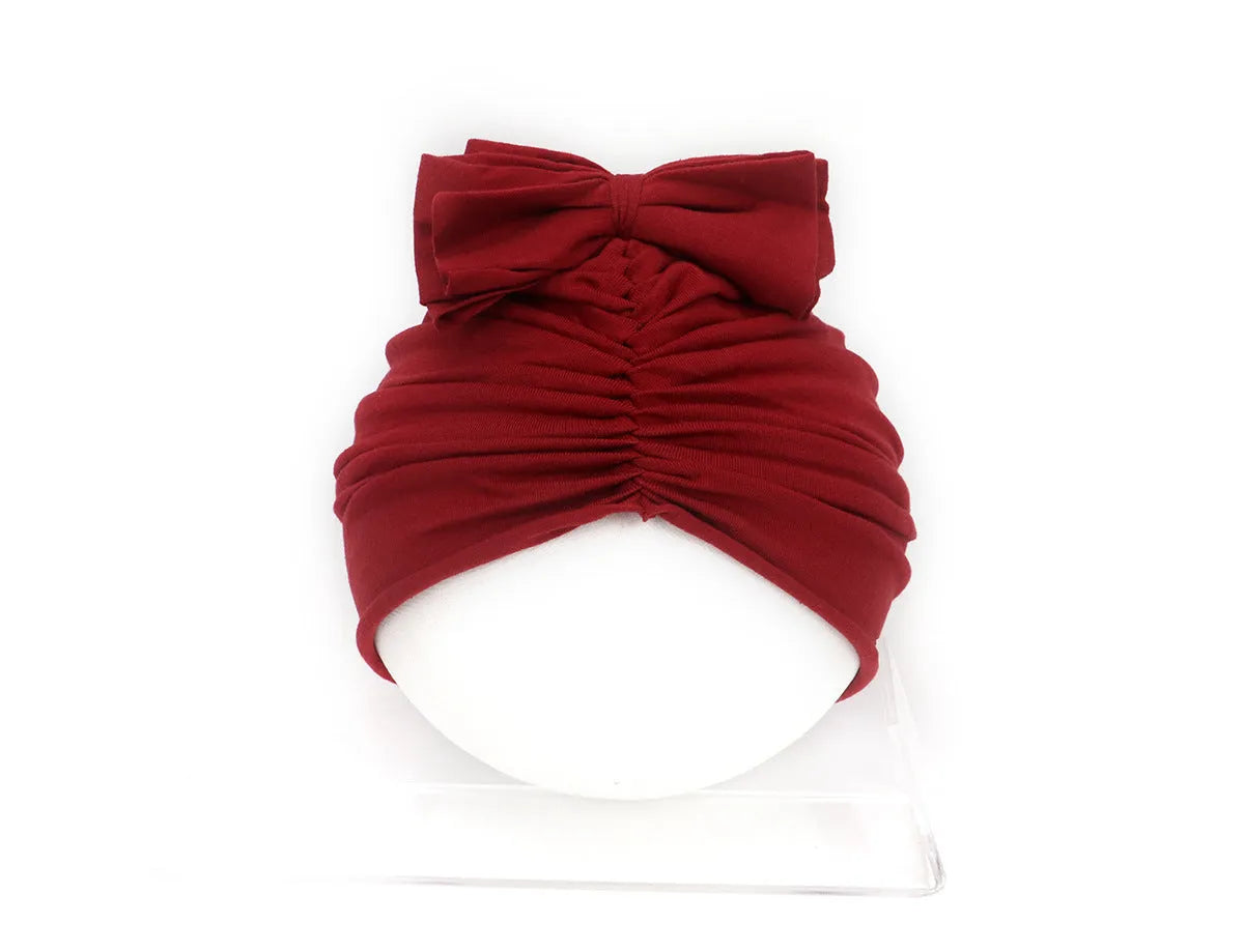 Soft acrylic knitted baby girl turban hat in a solid colour, shown on an infant