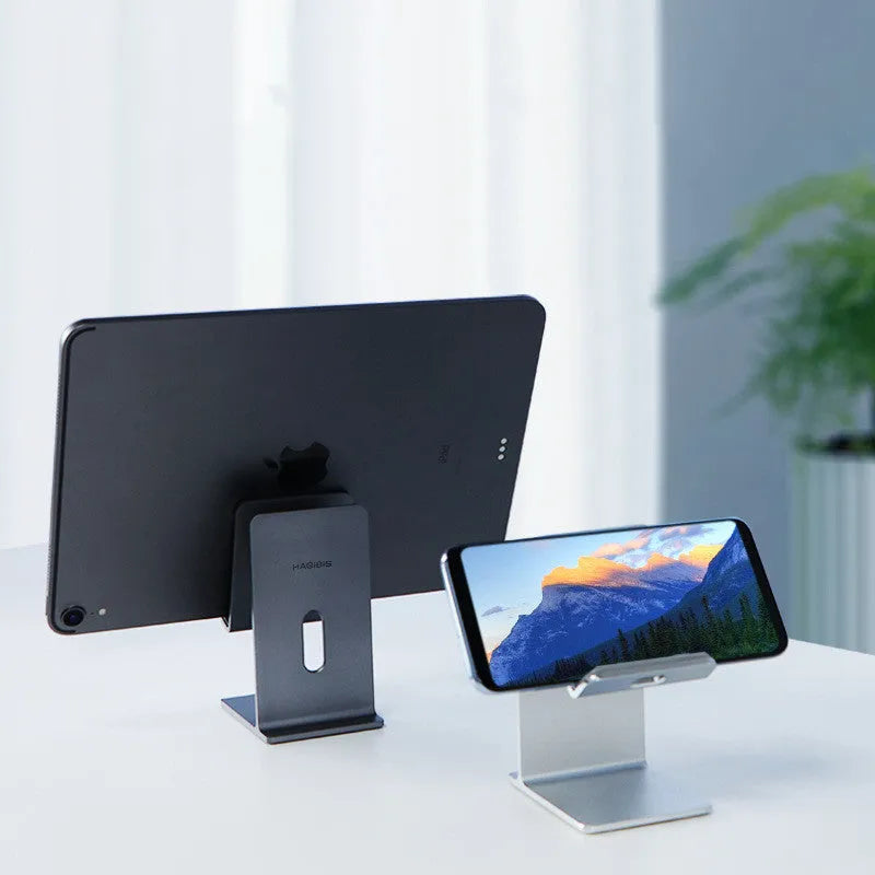 Alloy mobile phone and tablet holder stand in dark space grey and silver on a desktop.