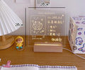 White decorative LED bedside night light with a writable message board on a wooden nightstand.