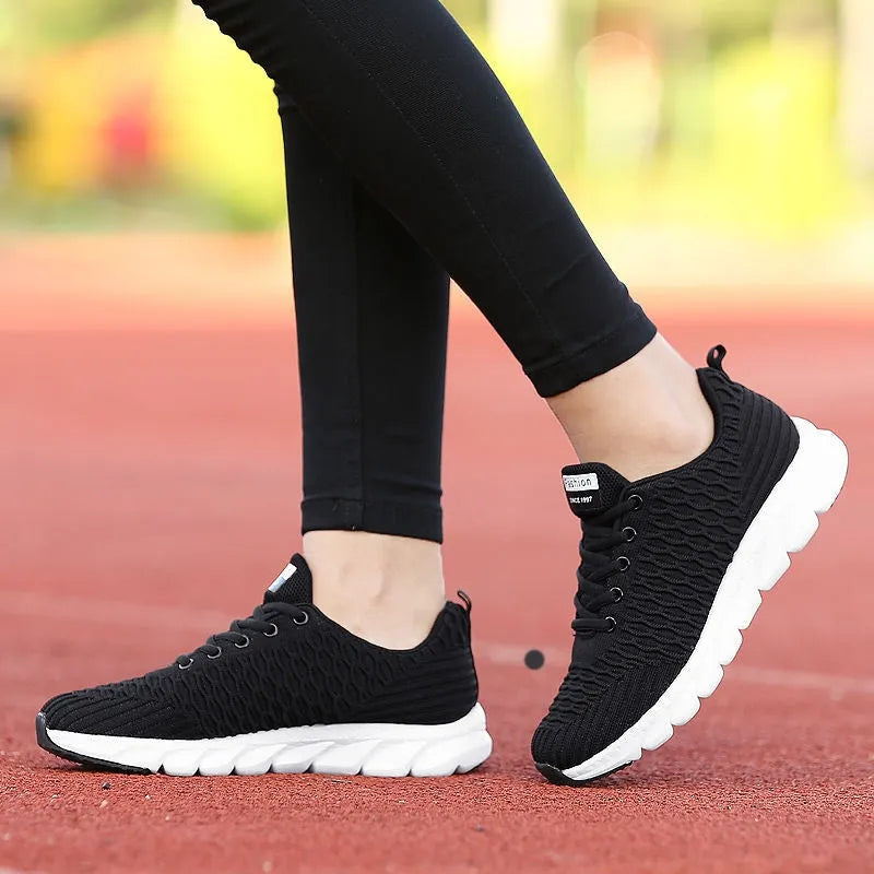 Women's running shoes in black, pink, or white with a breathable fly knit upper and durable outsole.
