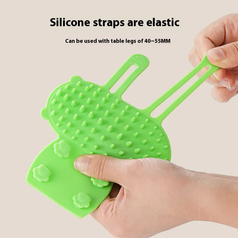 Silicone cat grooming comb with adjustable strap mounted on table leg, showing rounded teeth for pet hair removal