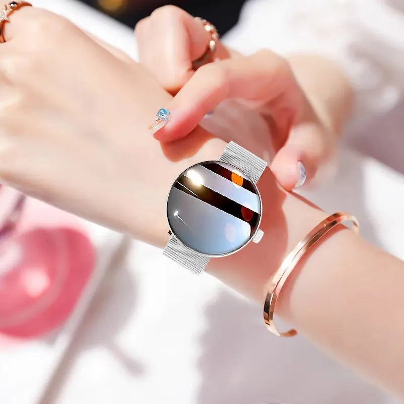 Circular women's smartwatch with metal strap and colour touchscreen display on a wrist.