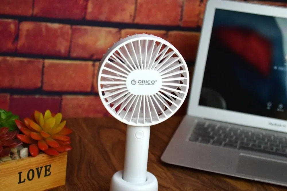 White ORICO FH1 portable USB desk and handheld fan with rechargeable battery on a wooden table.
