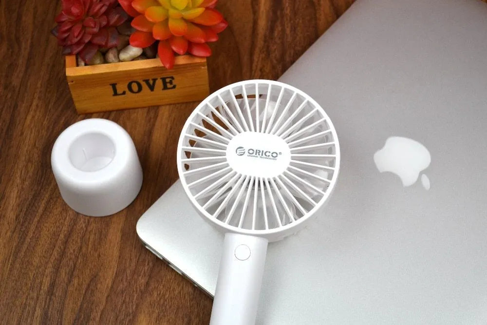 White ORICO FH1 portable USB desk and handheld fan with rechargeable battery on a wooden table.