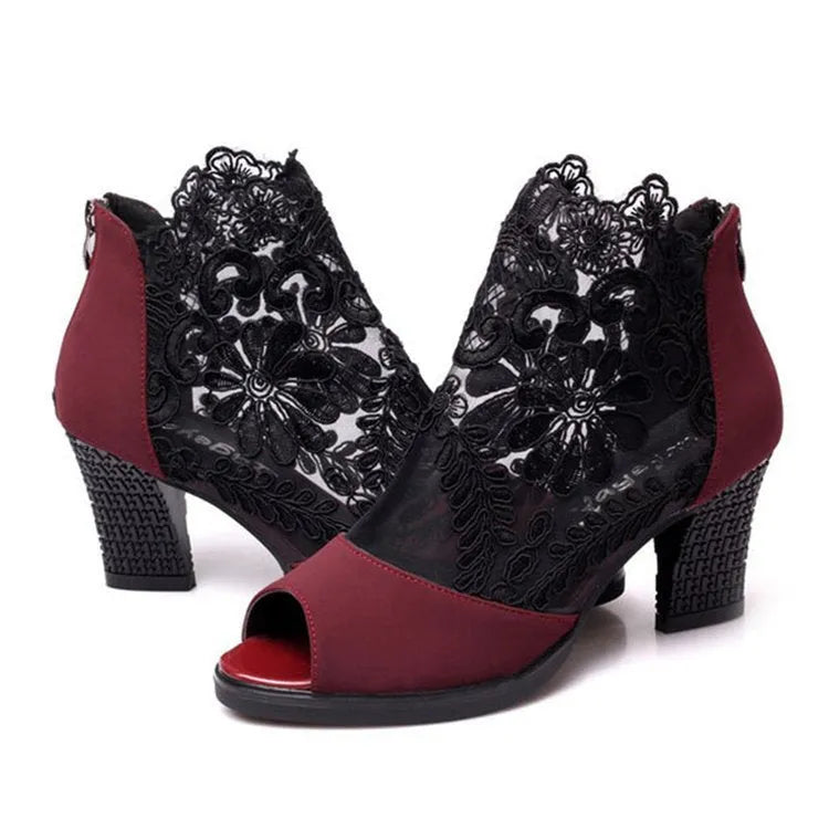 Black women's gladiator sandals with lace upper, square high heel, and side zip closure on a foot.