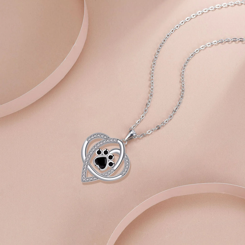 Close-up of a copper pendant necklace showing a charm with dog paw and cat footprint designs on a cross chain.