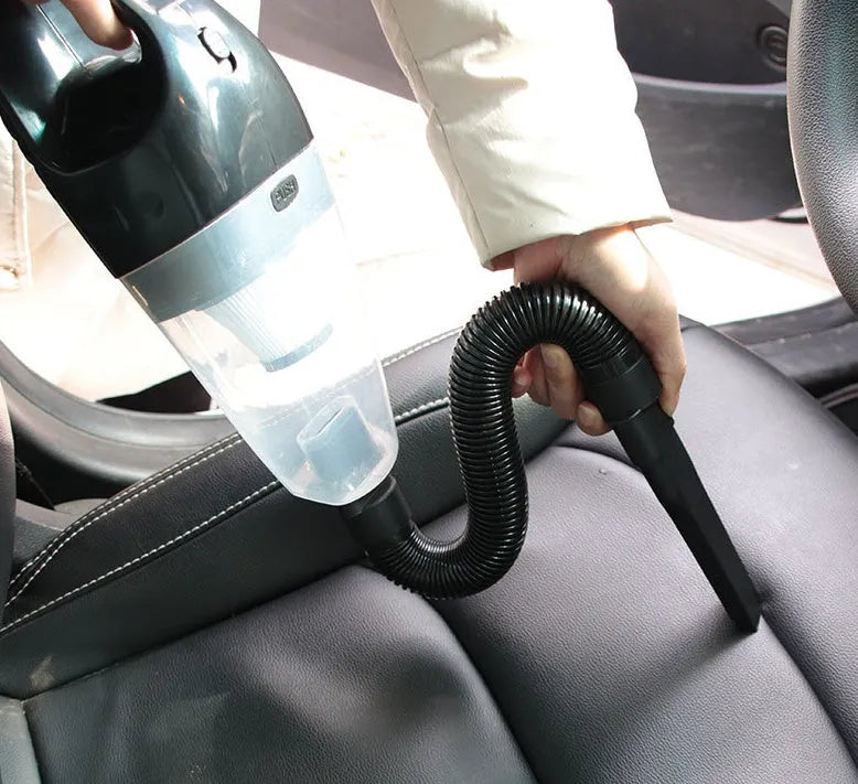 Orange handheld car vacuum cleaner with nozzle attachments and a coiled power cord, showing scale next to a car seat.