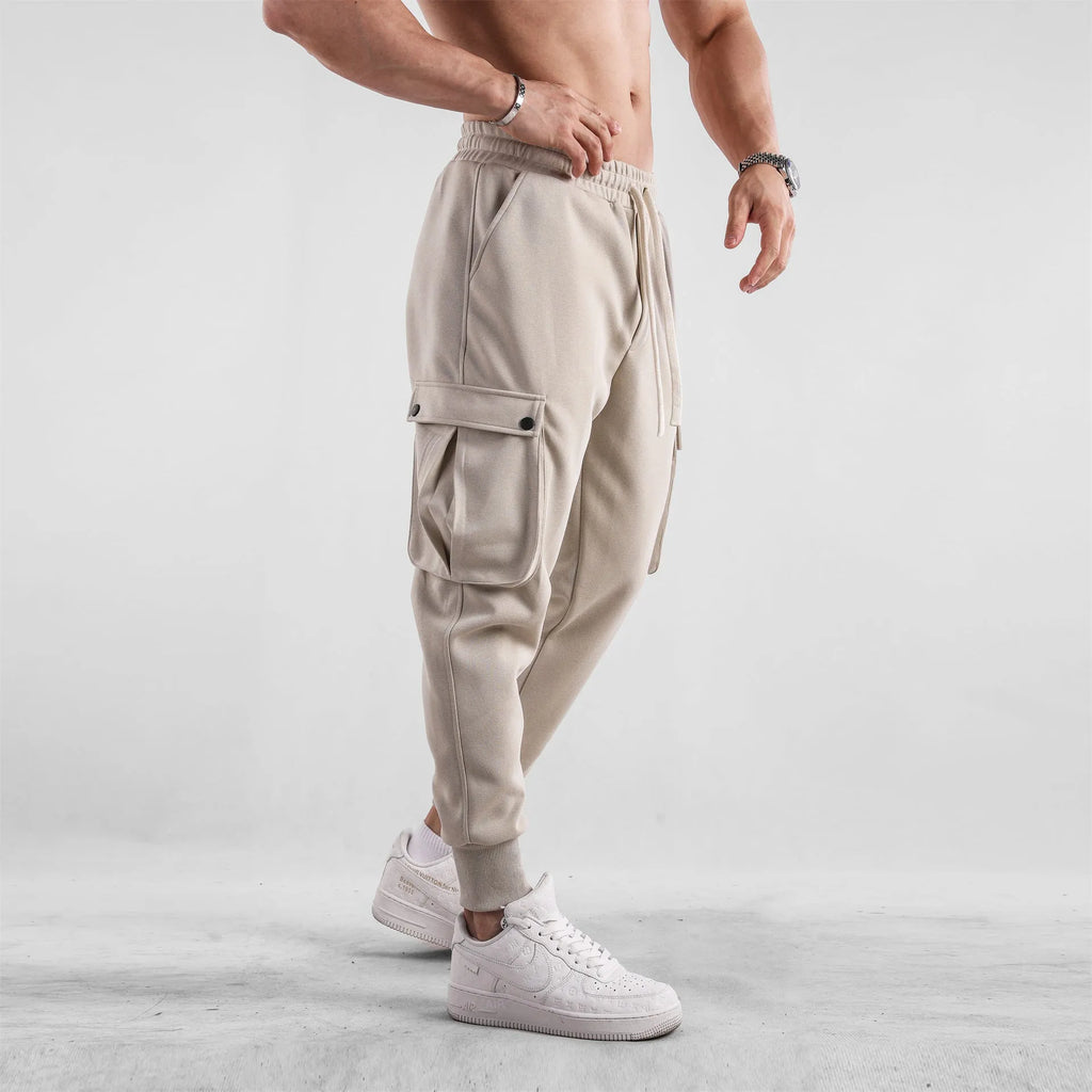 Men's loose light grey cotton sports trousers with ankle ties and multiple pockets laid flat.