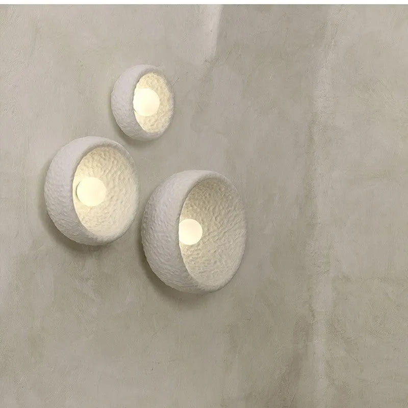 Japanese modern simple wall lamp with white resin shade in three size options on a plain wall.