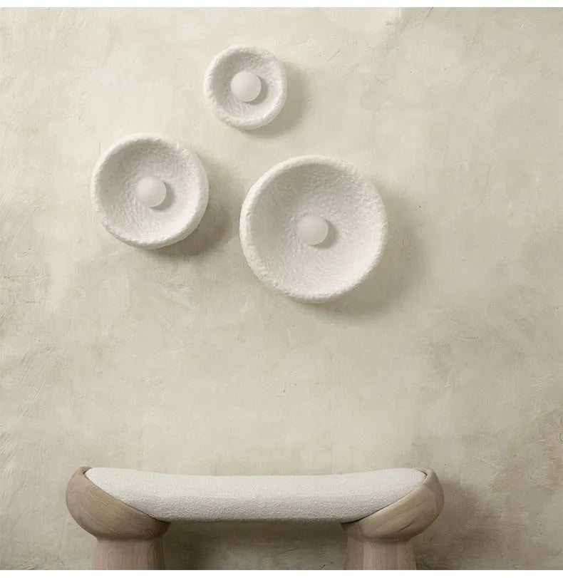 Japanese modern simple wall lamp with white resin shade in three size options on a plain wall.