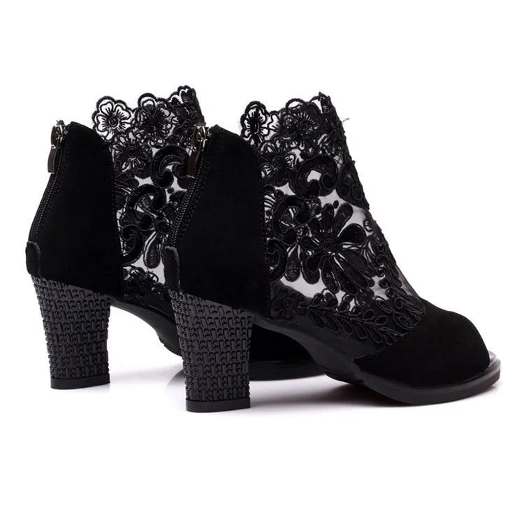 Black women's gladiator sandals with lace upper, square high heel, and side zip closure on a foot.