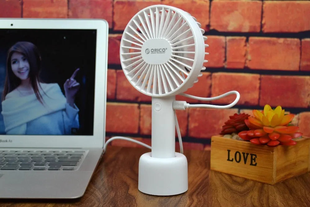 White ORICO FH1 portable USB desk and handheld fan with rechargeable battery on a wooden table.