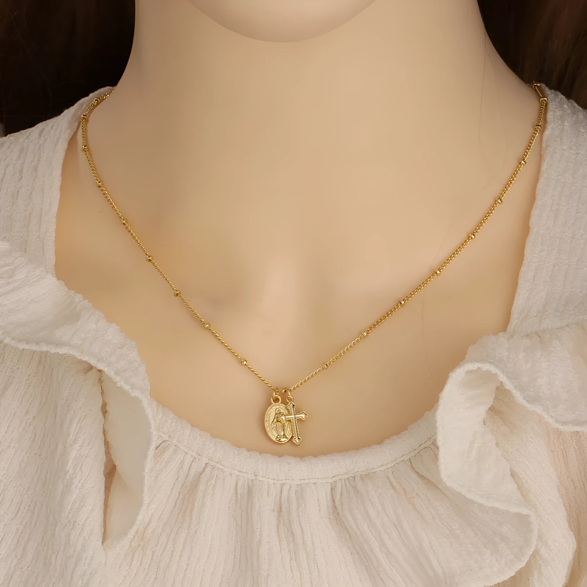 Gold geometric cross pendant necklace with Virgin Mary design on a chain.