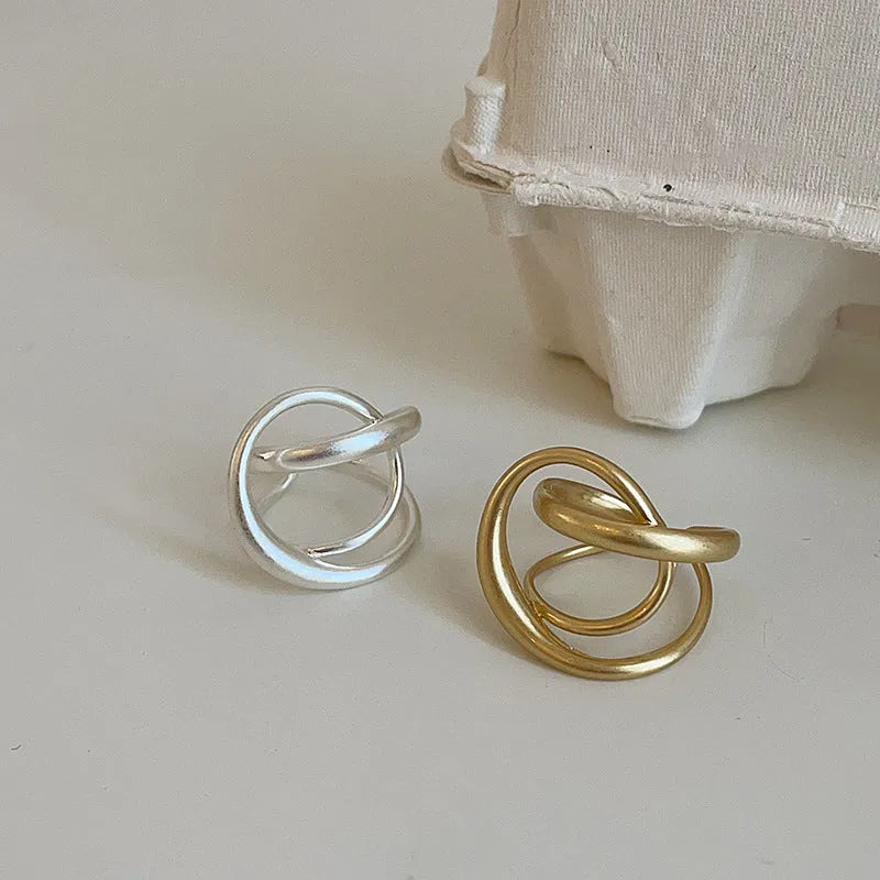 Geometric open ring for women with three-dimensional interlaced design in matte gold or silver metal.