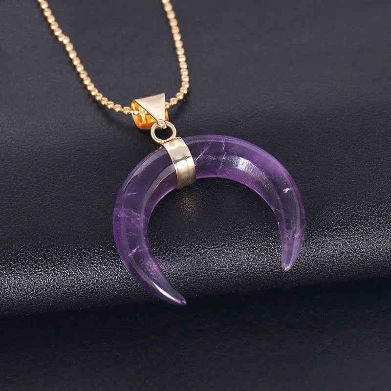 A pink semi-precious stone moon pendant on a copper-coloured chain, laid flat.