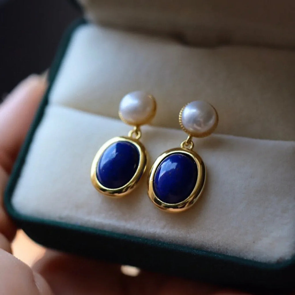 A pair of simple stud earrings with blue lapis lazuli pearls set in silver backings featuring auspicious patterns.