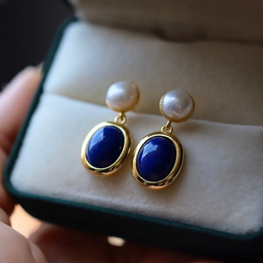 A pair of simple stud earrings with blue lapis lazuli pearls set in silver backings featuring auspicious patterns.