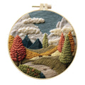 Landscape embroidery DIY kit with cotton fabric, printed pattern, embroidery frame, needles, and thread on wooden surface