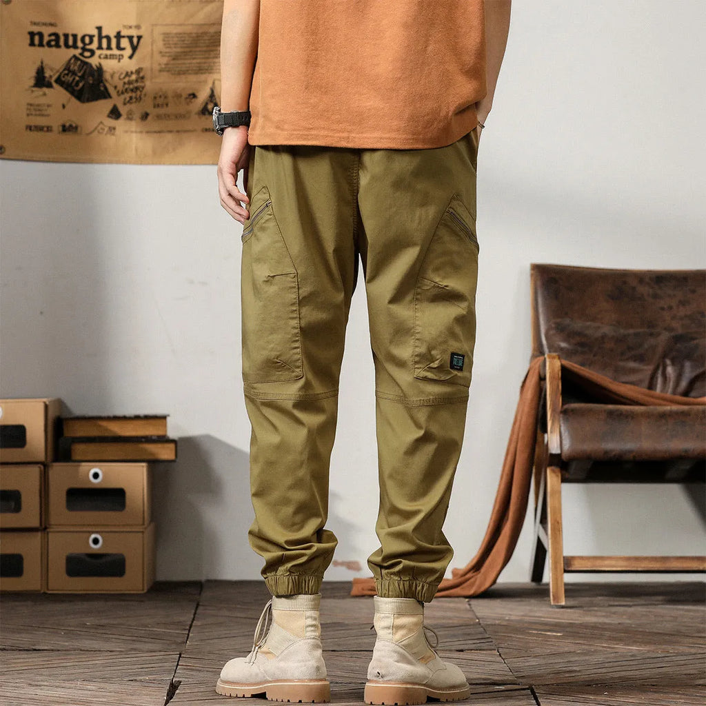 Men's loose cotton harem pants in khaki with a tapered ankle opening and zip fly.