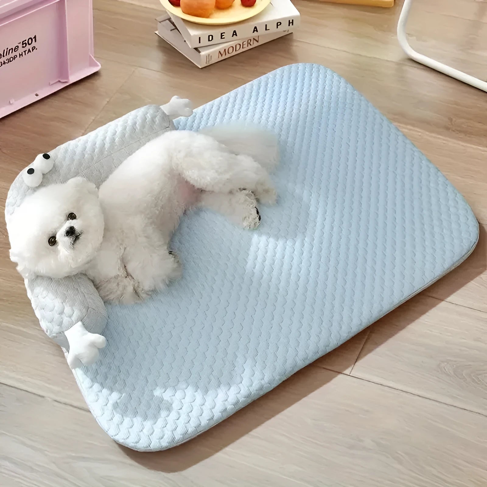 Blue pet cooling mat with big-eyed monster print on a wooden floor