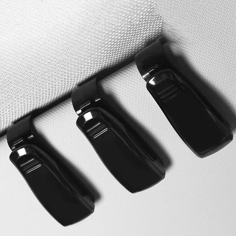 Black plastic car sun visor clip holding a pair of sunglasses and a parking ticket.