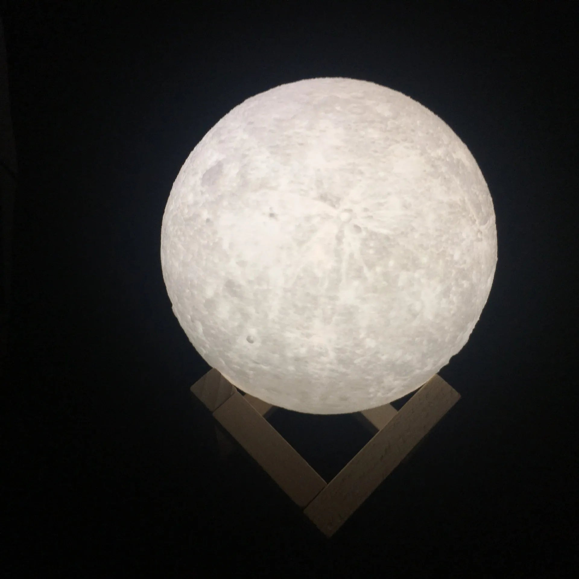 3D printed white moon lamp on a wooden stand, showing detailed craters and soft LED glow.