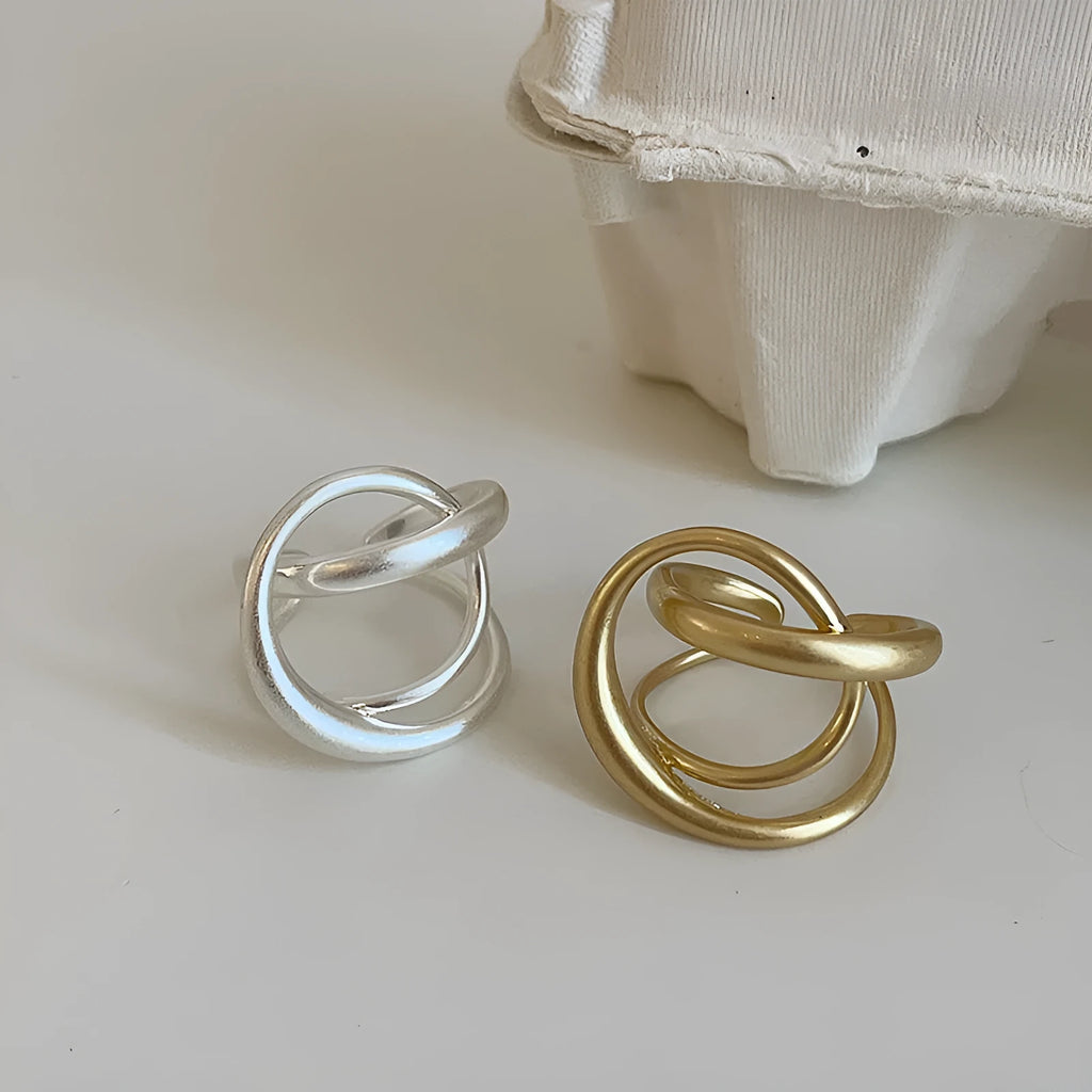 Geometric open ring for women with three-dimensional interlaced design in matte gold or silver metal.