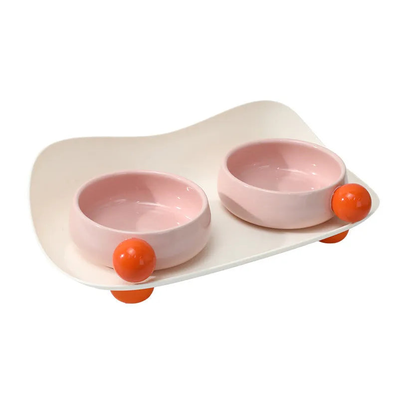 Raised ceramic double pet feeding bowl in pink, yellow, and pink yellow colour options on a floor.