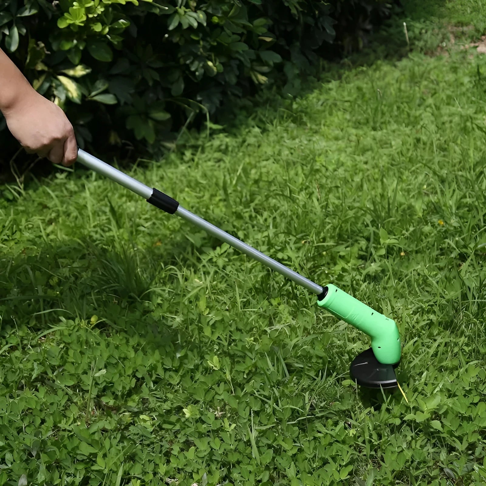 Cordless lawn trimmer with extension pole and protective shield on grass