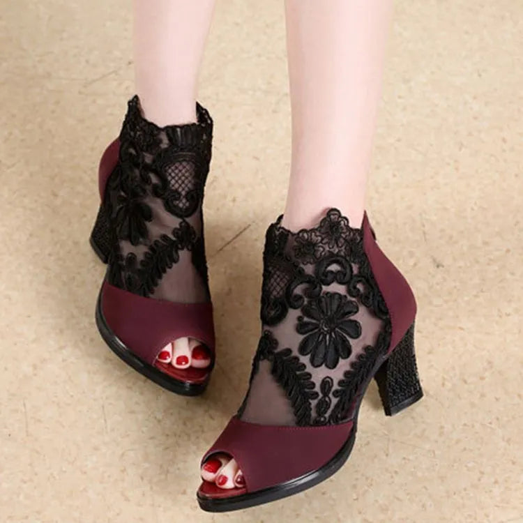 Black women's gladiator sandals with lace upper, square high heel, and side zip closure on a foot.