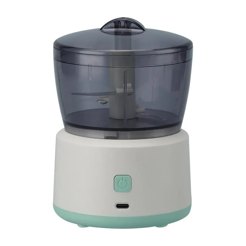White mini electric meat grinder with transparent cup and stainless steel blades on a kitchen worktop