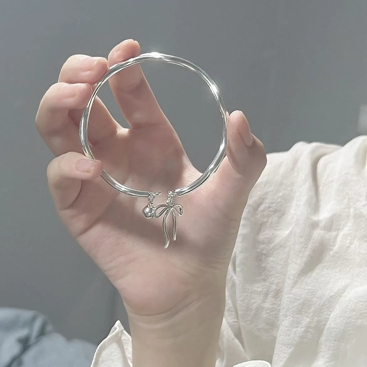 Silver bow bracelet with adjustable bell clasp on wrist, showing M1534 electroplated finish