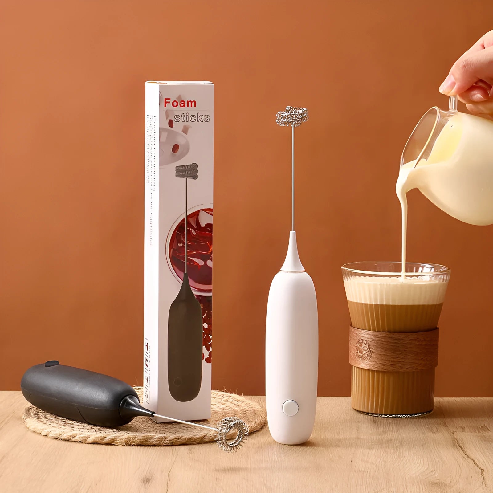 A black and a white hand-held electric milk frother for coffee, displayed on a kitchen counter.