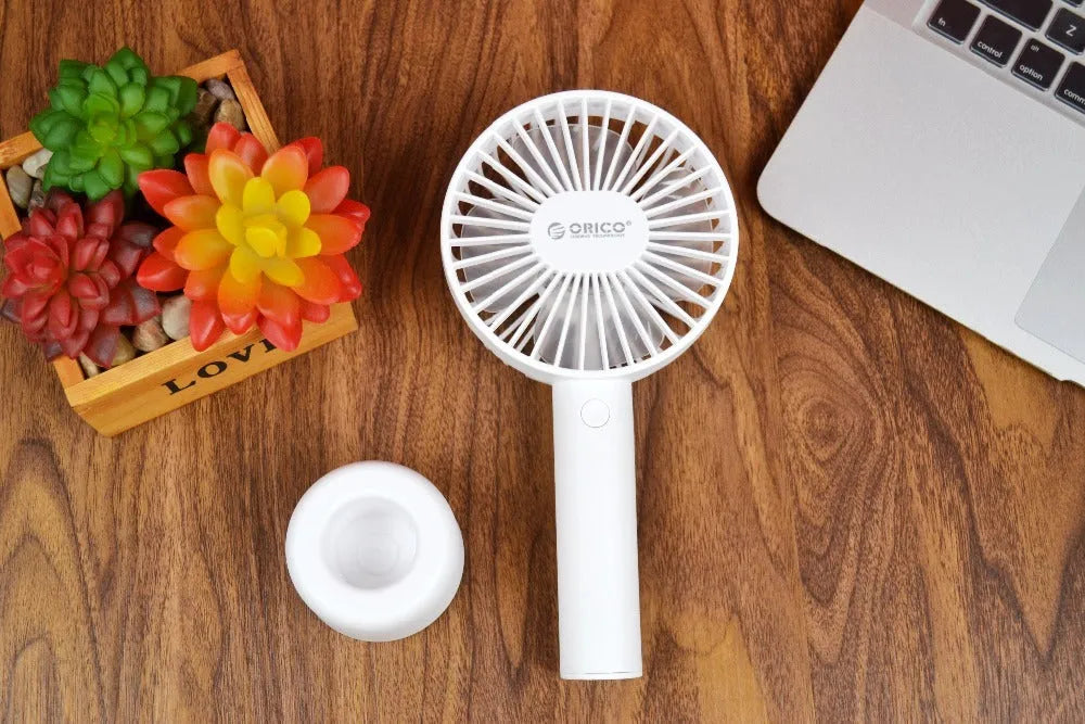 White ORICO FH1 portable USB desk and handheld fan with rechargeable battery on a wooden table.