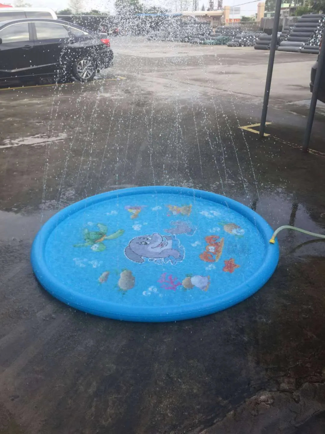 Blue PVC children's water spray mat with marine animal prints connected to garden hose