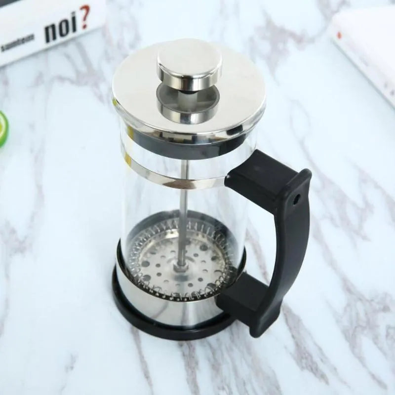 Compact stovetop moka pot coffee maker with glass top and stainless steel base.