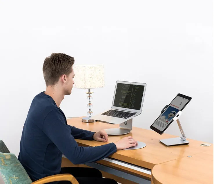 Black foldable aluminium phone and tablet stand with 360-degree rotation on a wooden desk