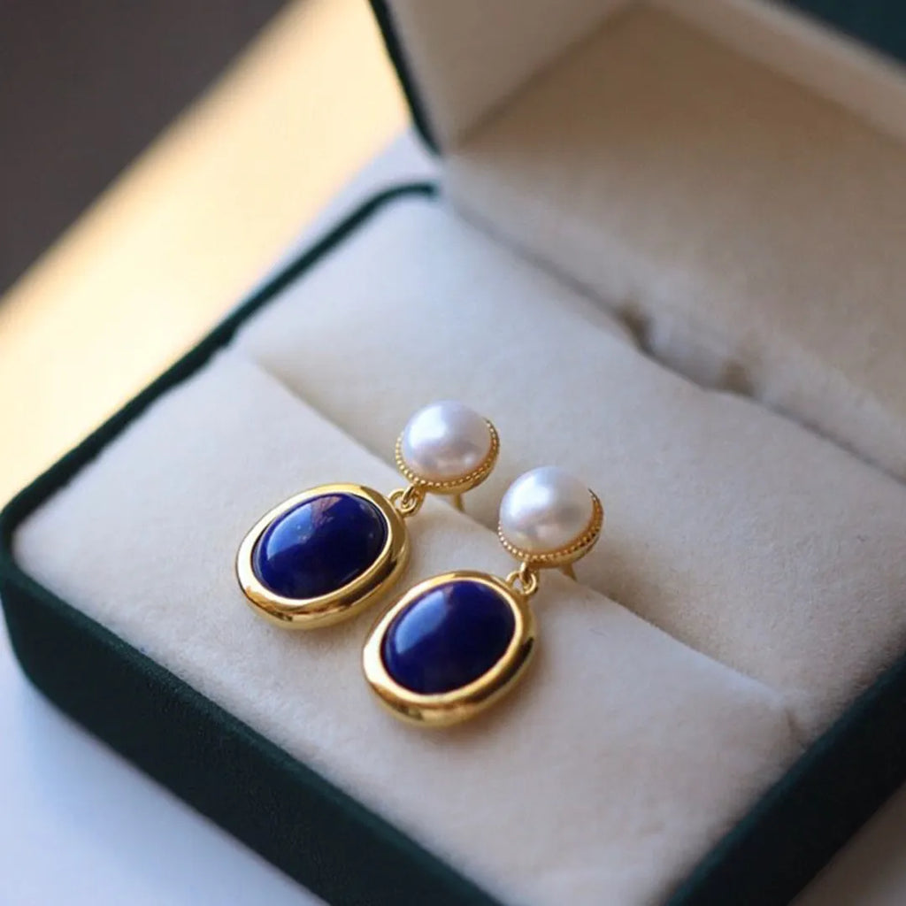 A pair of simple stud earrings with blue lapis lazuli pearls set in silver backings featuring auspicious patterns.