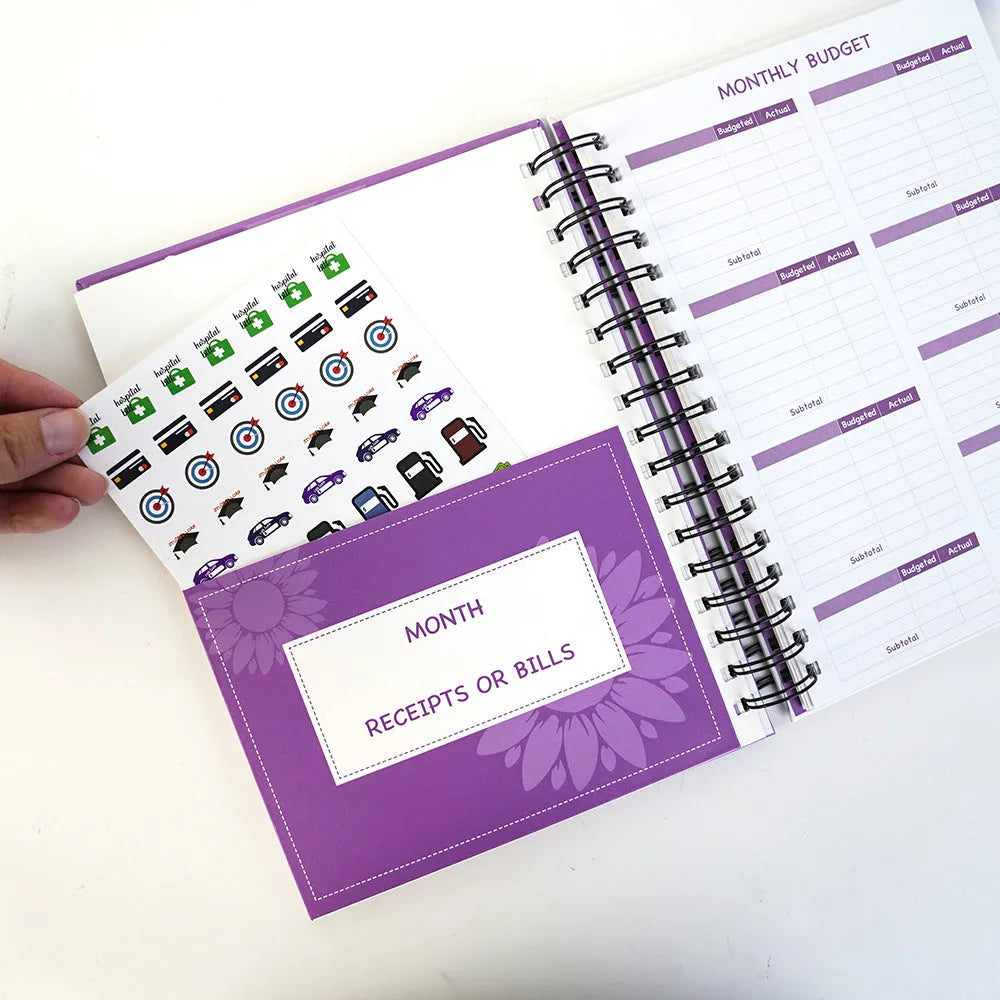 Purple coil-bound financial planning notebook with budget stickers and paper clips on A5 page